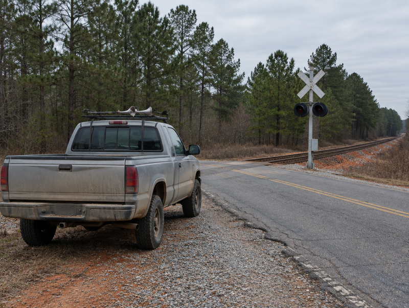 Dusty pickup truck with roof-mounted air horns stopped near a rural railroad crossing with a crossbuck and signal mast