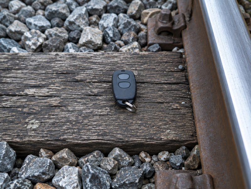 A small key-fob remote lying on a sleeper beside a polished rail