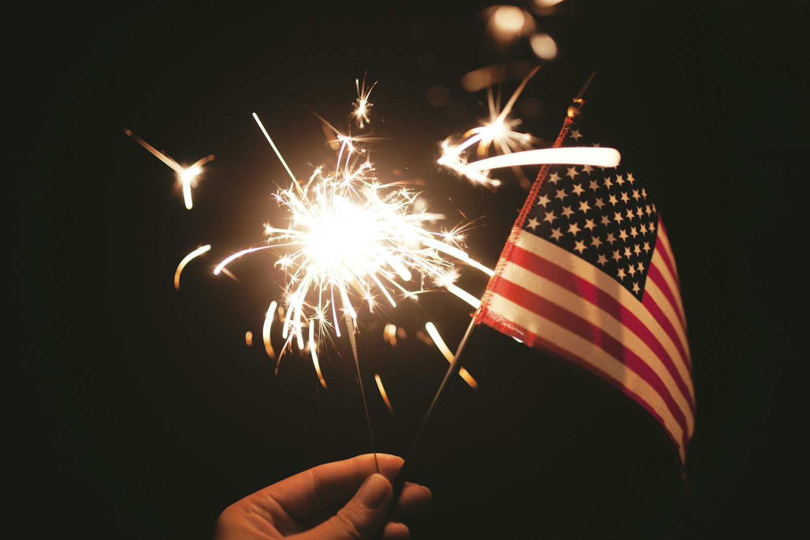 Bright sparklers throwing golden light beside an American flag at night during a Fourth of July Independence Day celebration