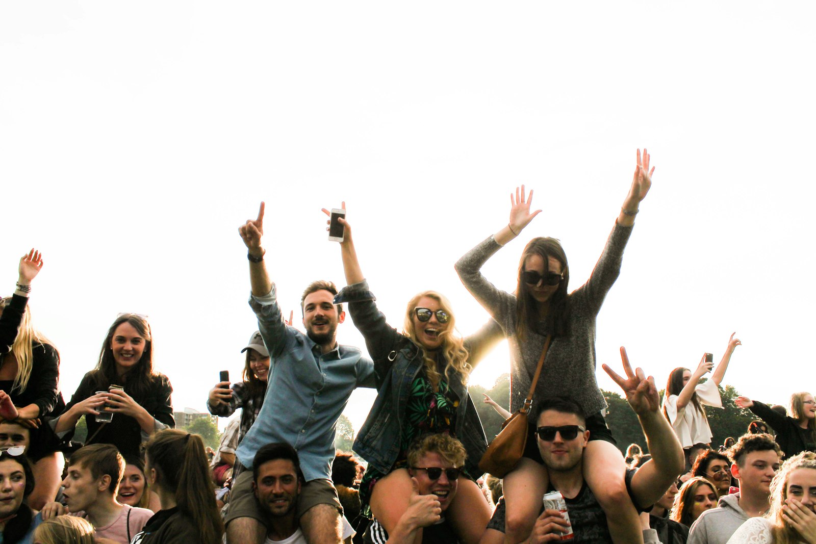 A daytime outdoor celebration with friends hoisting each other on their shoulders, arms raised in a cheering crowd — game-day energy among young people