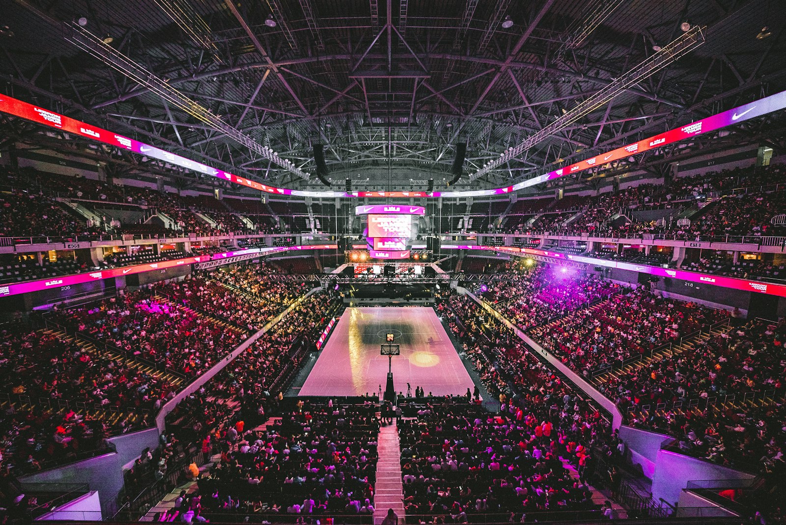 A packed basketball arena on game day, crowd surrounding the court under bright lights