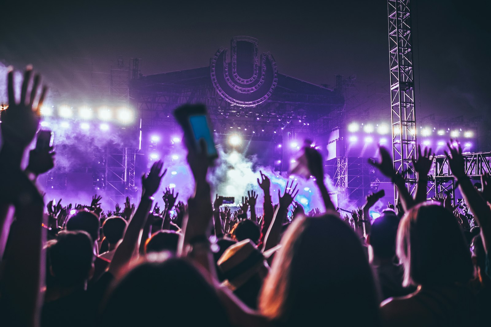 Festival crowd at dusk with hands raised toward an outdoor stage under stage lights