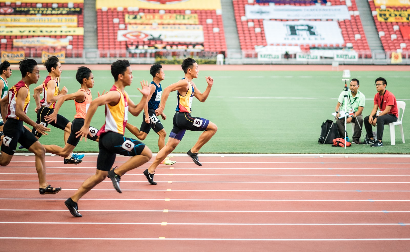 Runners sprinting down lanes on a red outdoor running track during a track and field meet