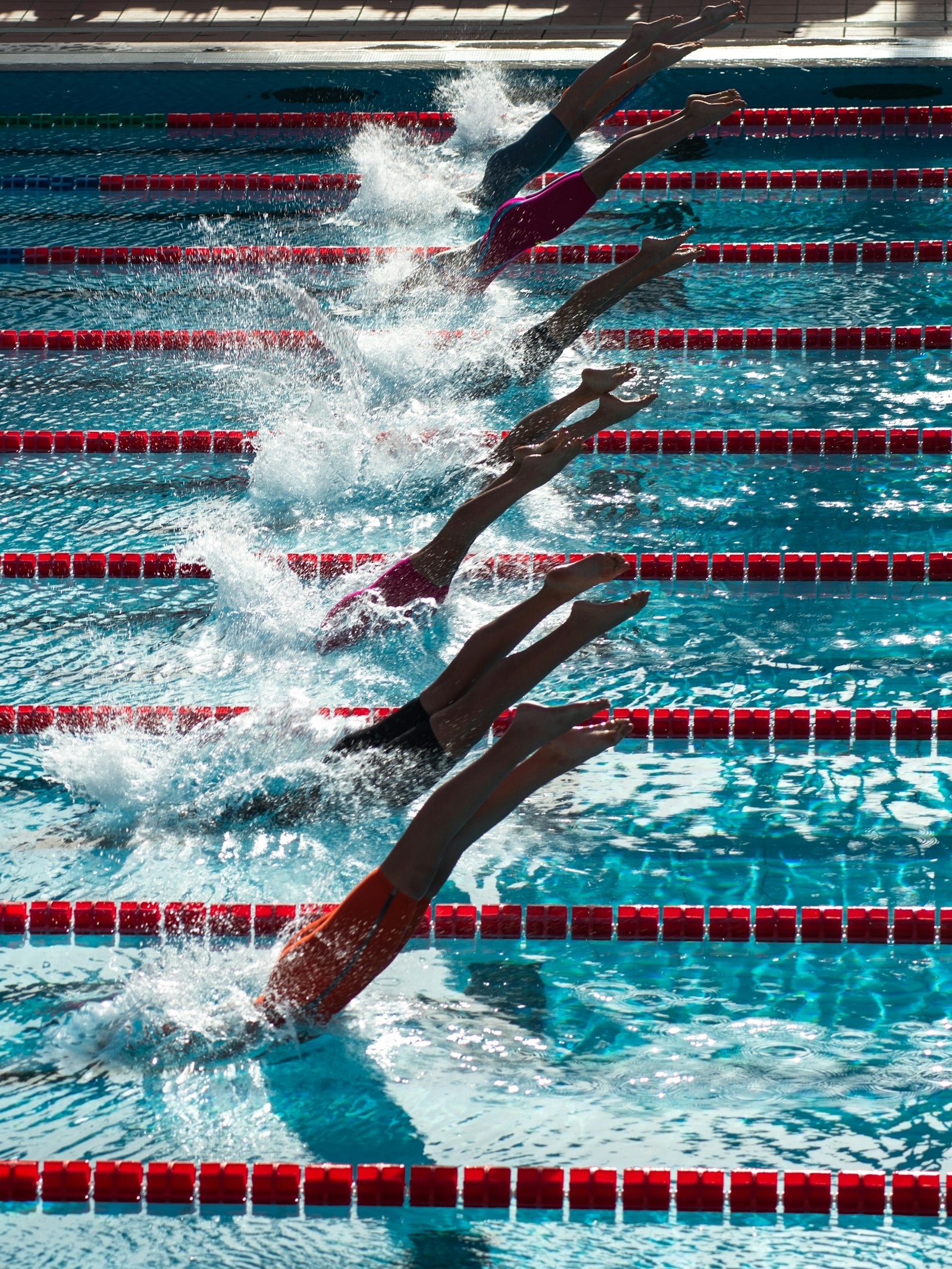 Swimmers racing across lanes in an outdoor competition pool during a daytime swim meet