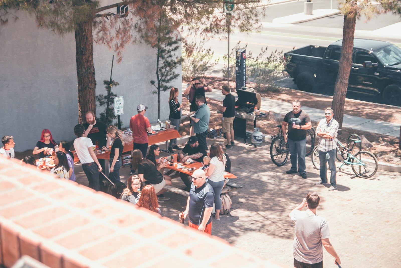 Neighbors gathered outdoors under trees at a summer block party with food and drinks on a sunny afternoon