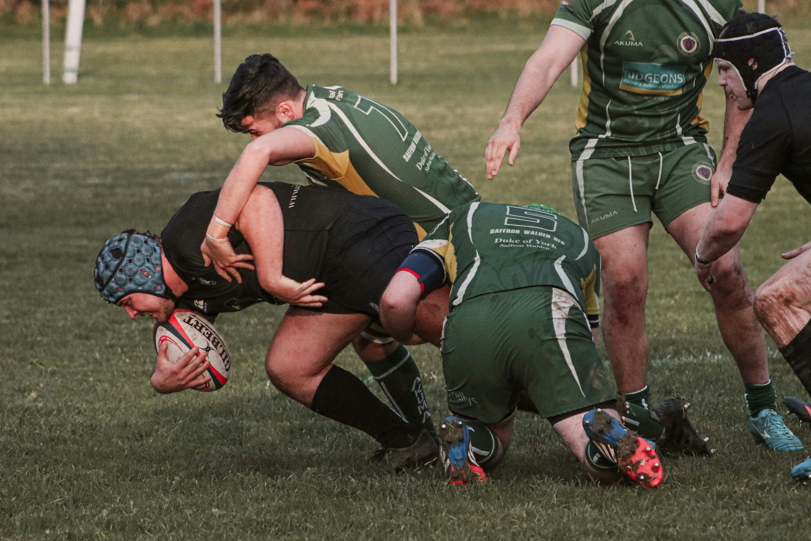Rugby players in kit colliding in a tackle on a grass pitch during a match