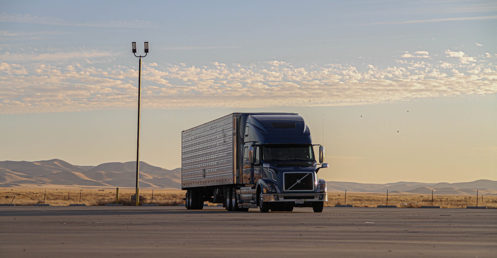 A dark semi truck hauling down an open desert highway under a clear daytime sky