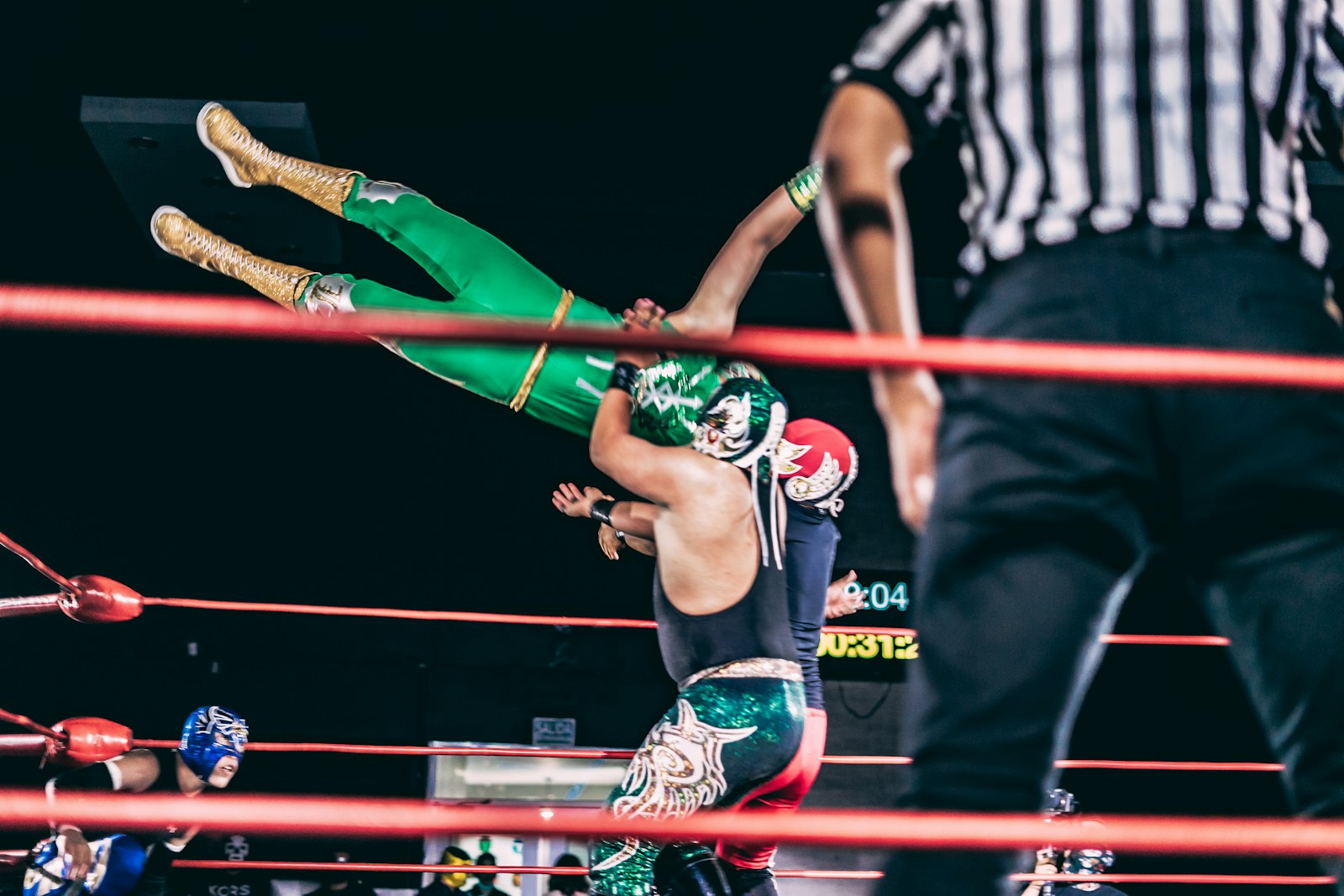 A wrestler hoisting an opponent overhead inside a brightly lit ring as a crowd watches ringside