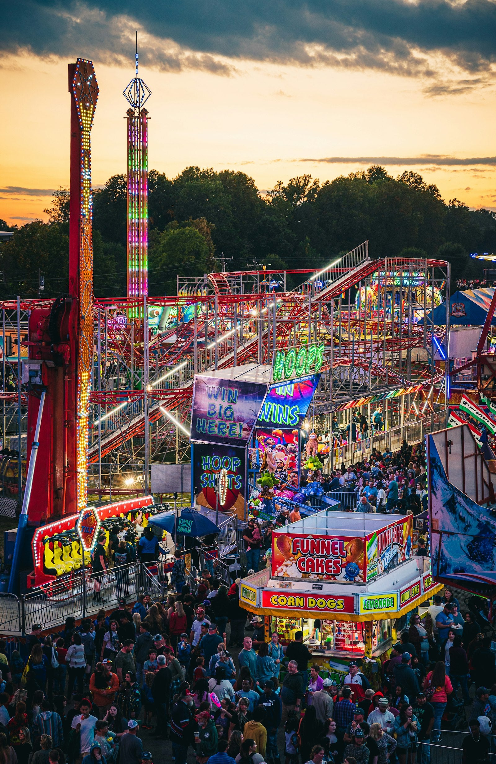 A county fairground full of carnival rides and a Ferris wheel seen from above at sunset