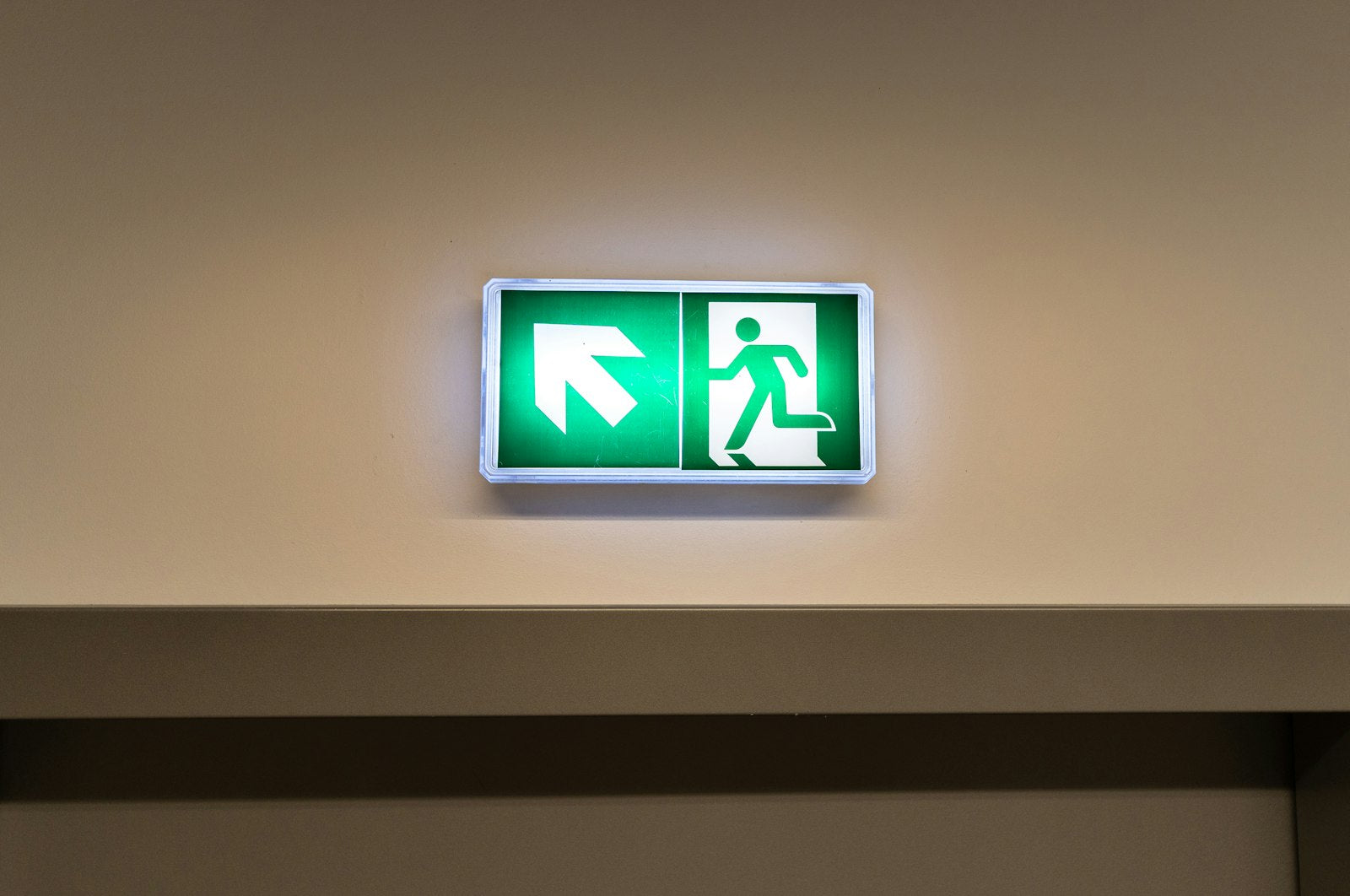 Illuminated green emergency exit sign with a directional arrow glowing above a doorway, marking the evacuation route out of a building