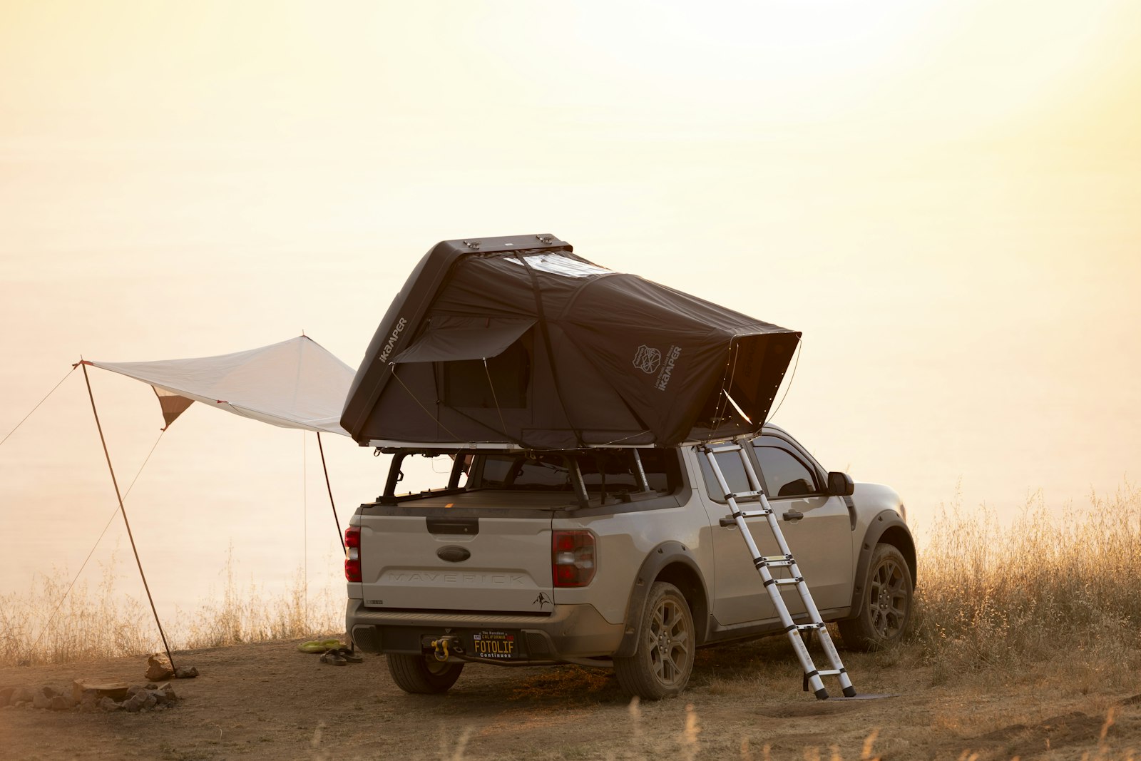 An overland pickup truck set up for camping with a rooftop tent mounted on the bed, parked in green wilderness on an overcast day