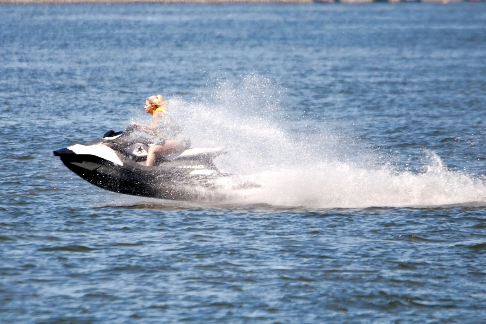 Rider on a jet ski carving across open water and throwing up a tall spray of spray in bright daylight
