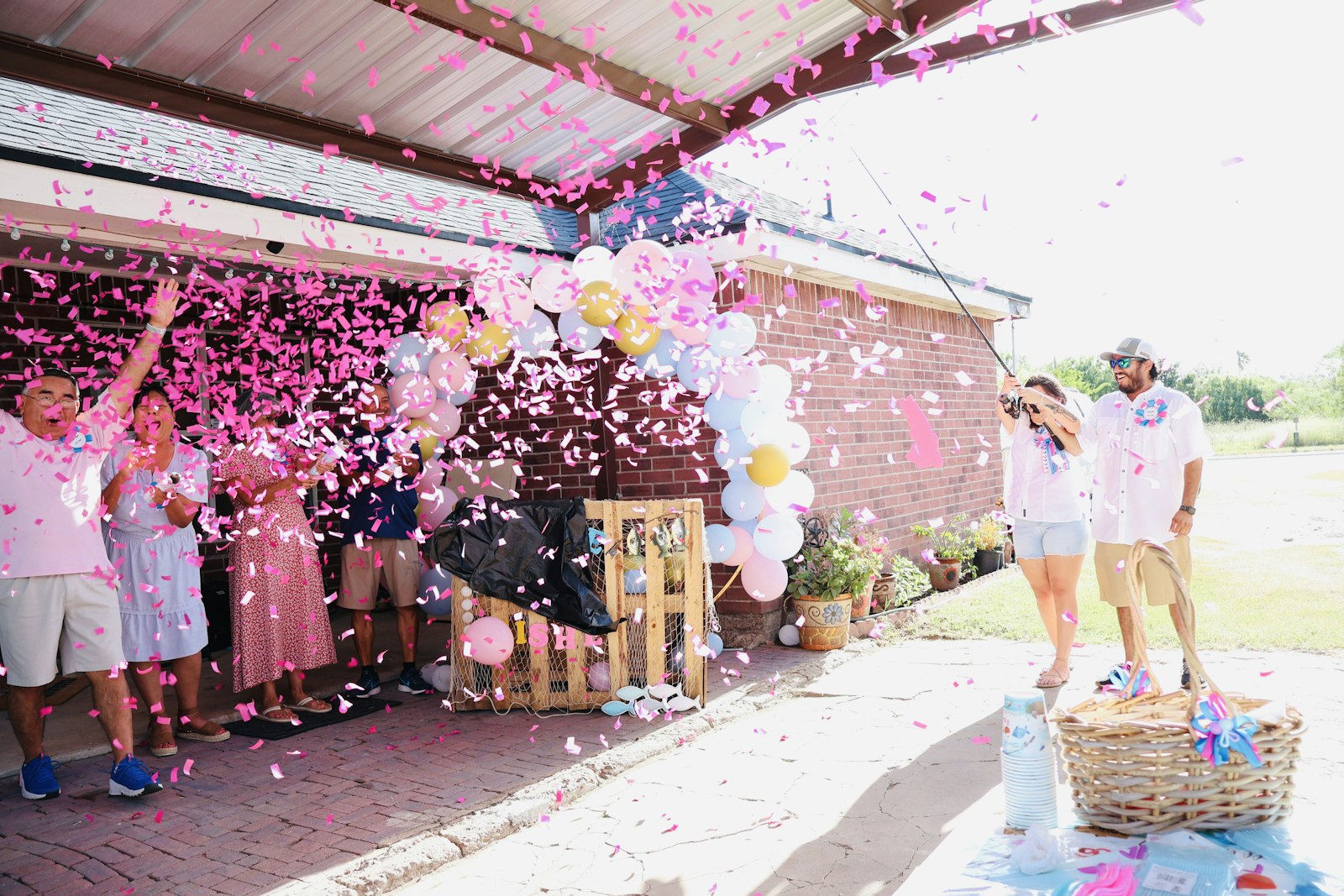 Group of people outdoors tossing pink confetti and balloons into the air during a celebration