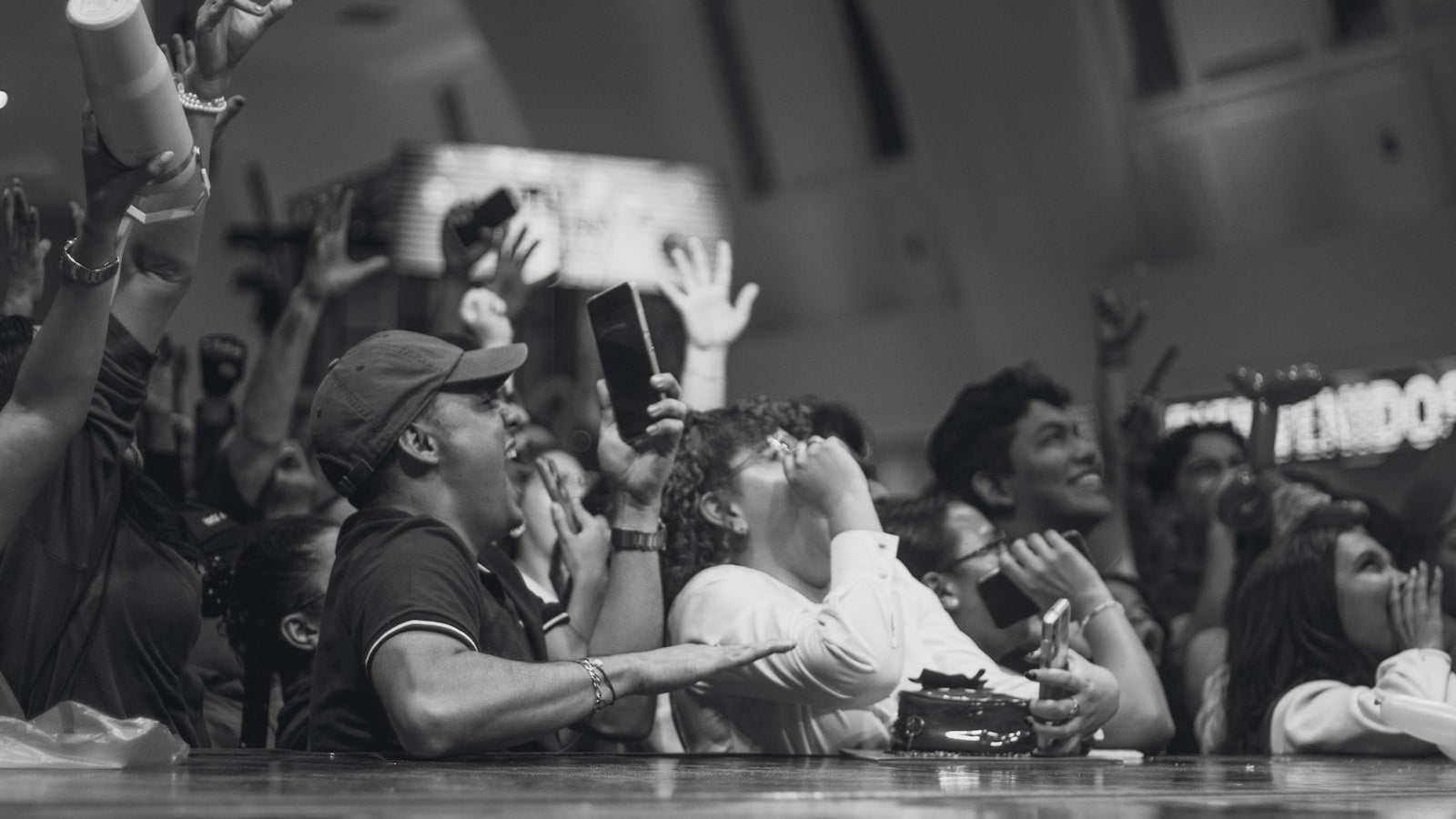 Outdoor crowd cheering with arms raised in the air, celebrating together at an energetic evening rally
