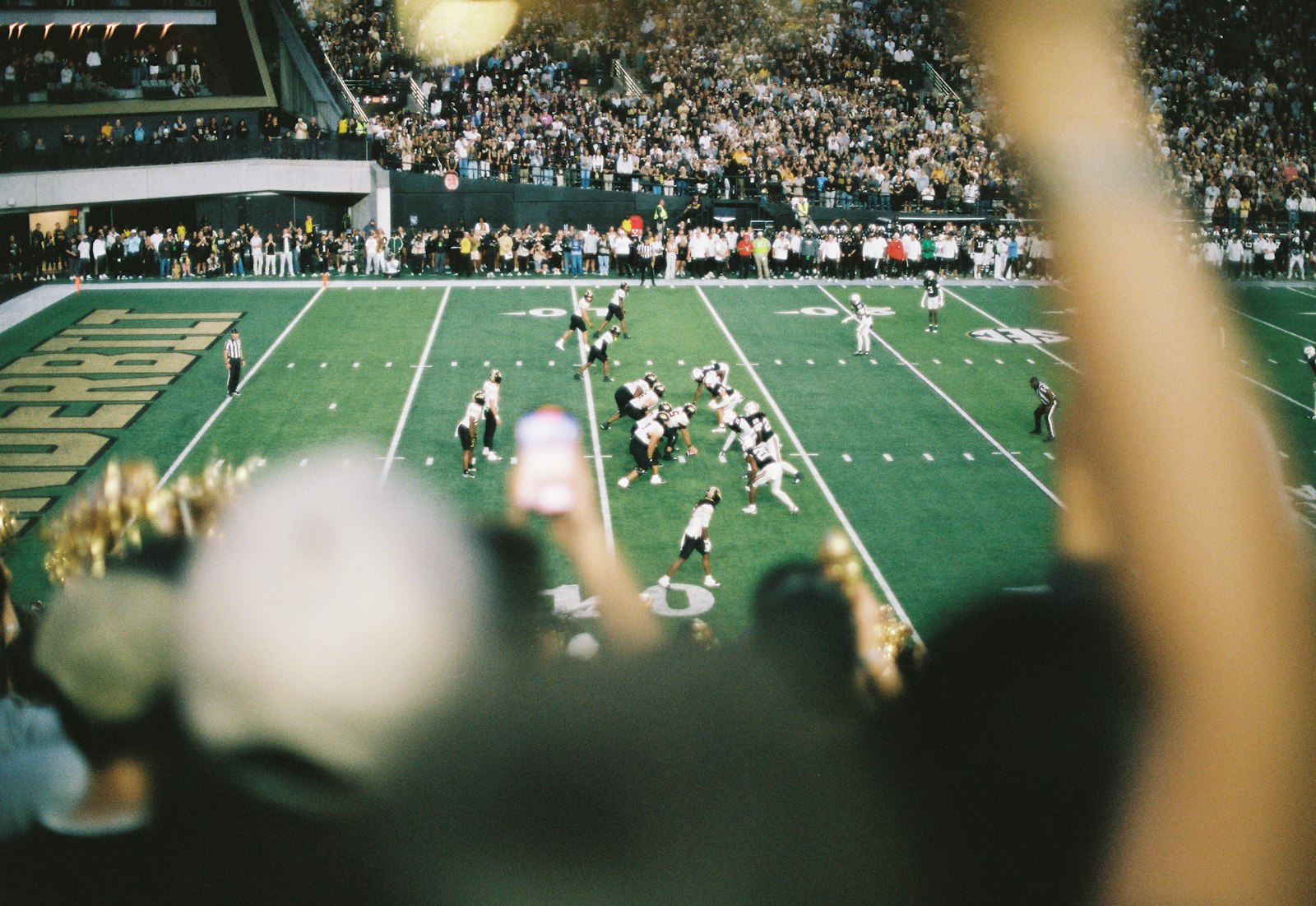 American football game under stadium lights with fans packed into the stands on a fall game day