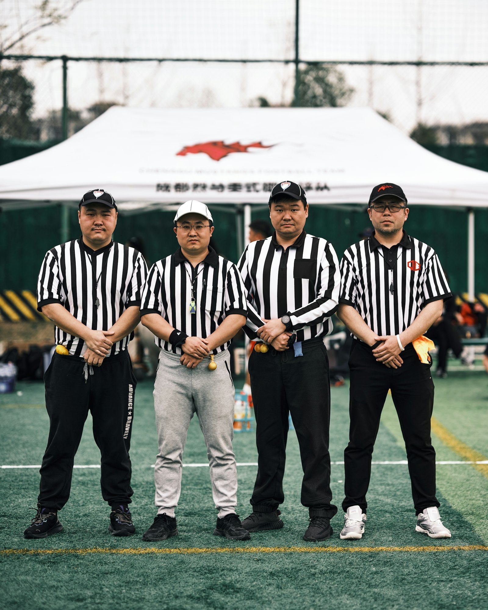 Four match officials in black-and-white striped referee uniforms standing together on an outdoor field before a game