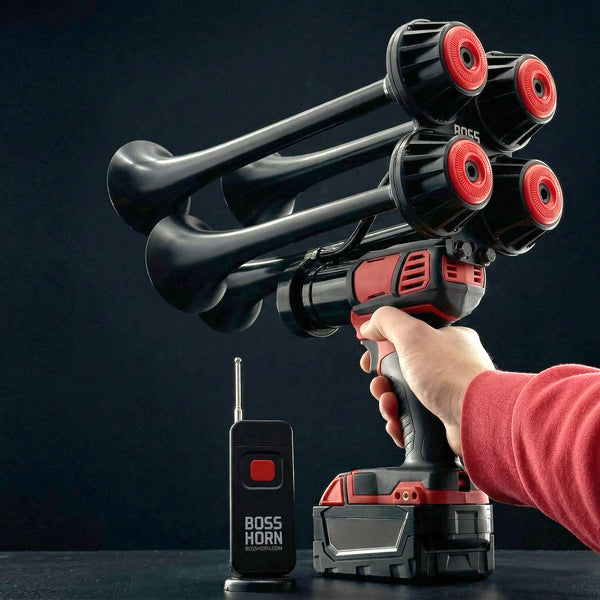 Hand holding a black and red horn device with multiple nozzles, remote control, and battery pack on a dark background.